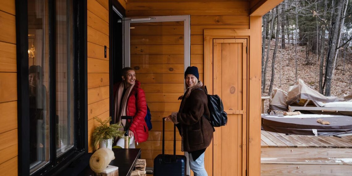 Two guests with luggage arriving at a wooden holiday cabin