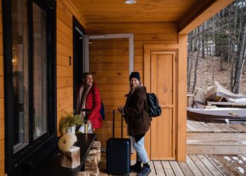 Two guests with luggage arriving at a wooden holiday cabin